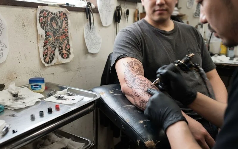 A detailed Japanese-style tattoo composition mid-session, showing wave and floral motifs being shaded on a forearm