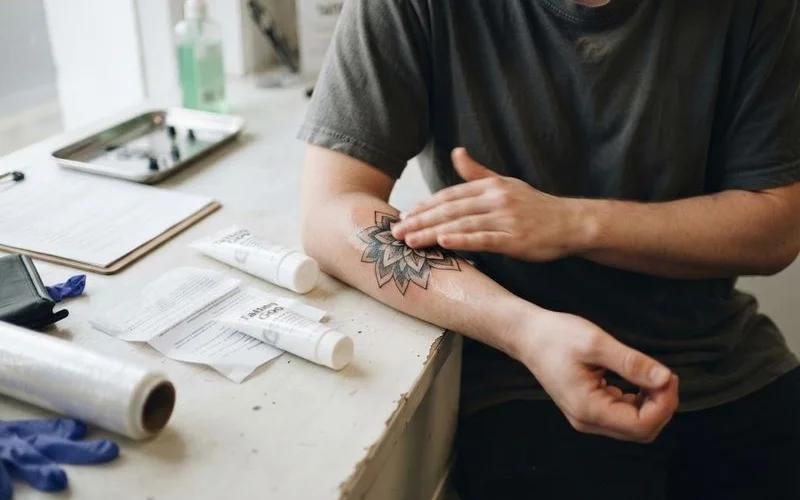 Someone applying a thin layer of aftercare moisturiser to a healing forearm tattoo, following studio instructions